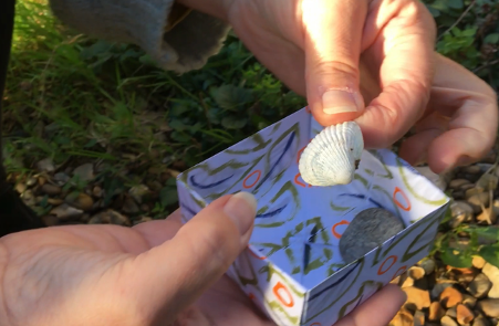 Someone's hands holding a small handmade box with a shell
