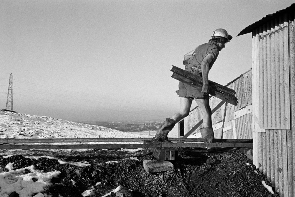 A black and white photograph of a miner carrying wood