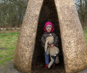  A young girl smiles while holding a rabbit inside Usagi Kannon, a giant bronze rabbit sculpture by Leiko Ikemura, at the Sculpture park. Photo by Kate Wolstenholme