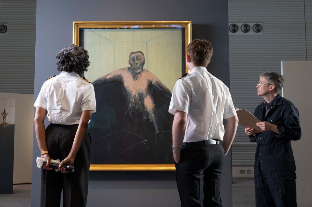 Two museum security guards and an administrator stand in front of a painting by Francis Bacon called Portrait of P.L., no.2 (1957)